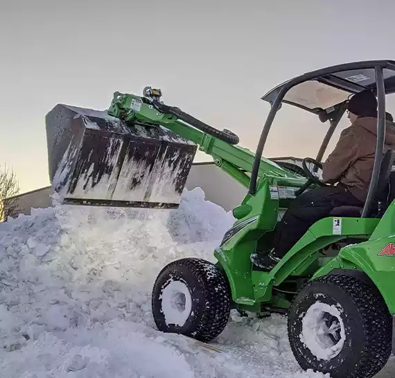 Commercial snow removal tractor clearing a parking lot in Utah winter by JC Property Maintenance